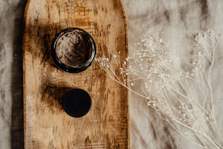 Top view of cosmetic clay mask on wooden tray with delicate dry flowers, ideal for skincare themes.